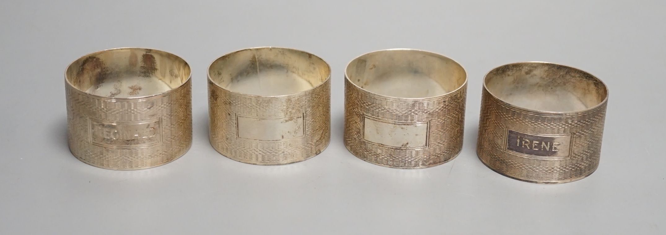 A set of four George VI engine turned silver napkin rings, H. Bros, Birmingham, 1943/4, two engraved with names.